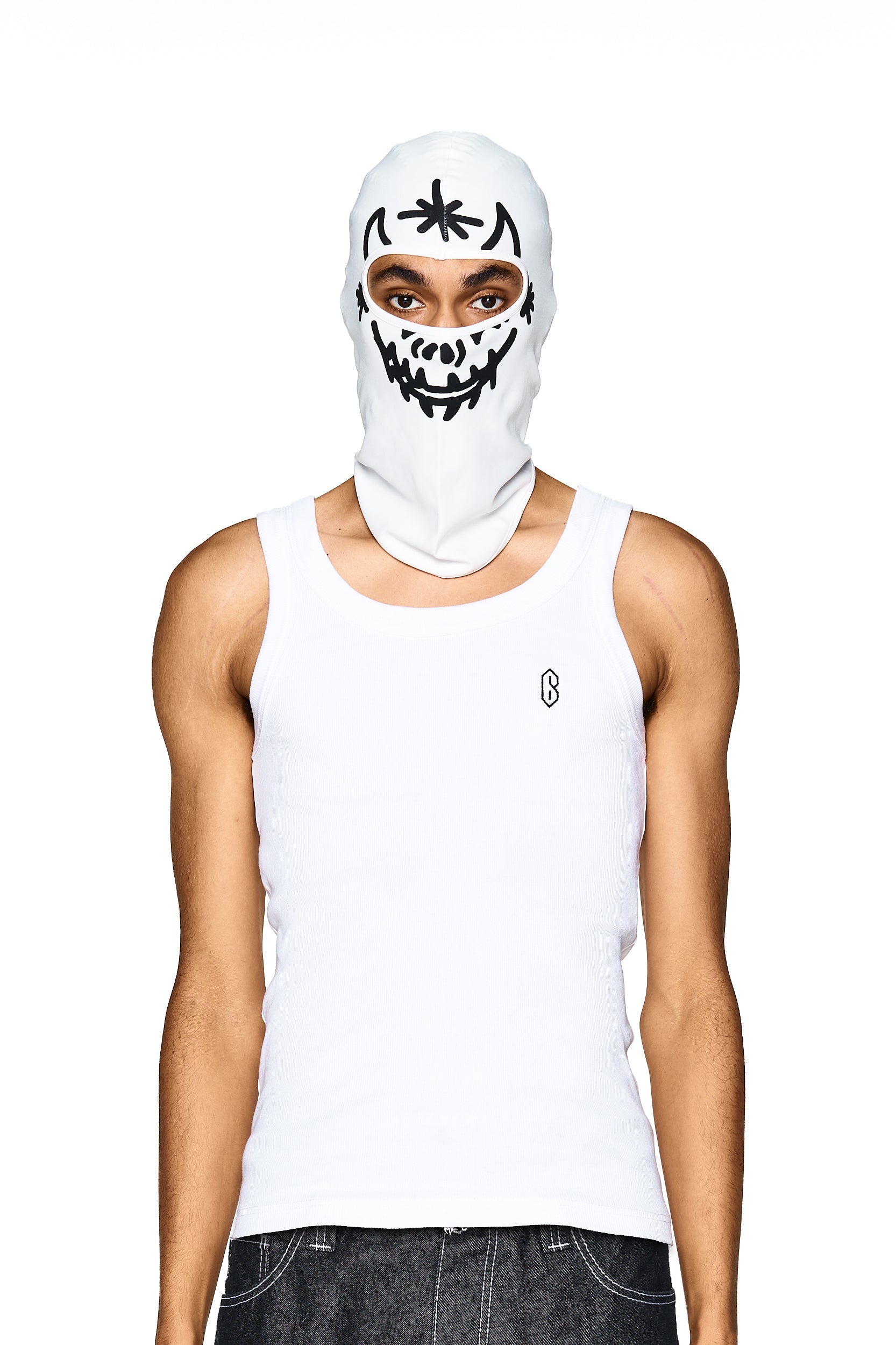 A person wears the 6PM F&F SKI MASK DEMON BALACLAVA WHITE—a white balaclava featuring a black cartoon face and star design—paired with a white tank top, standing against a white background.