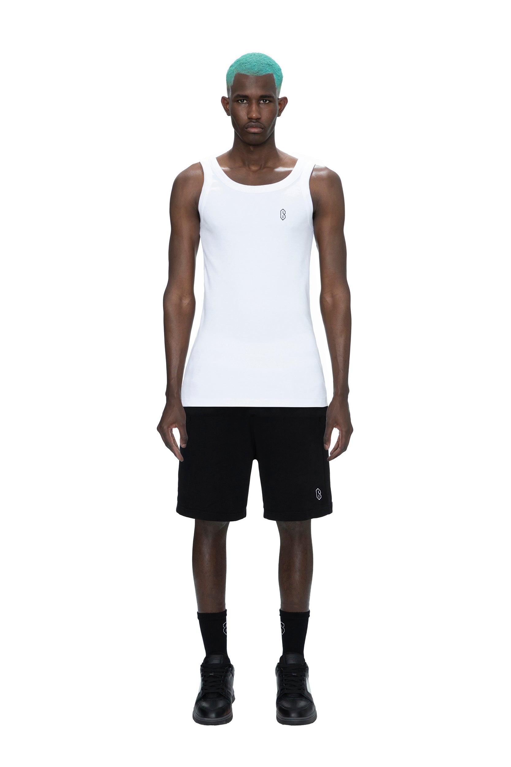 A person with teal hair wears a white sleeveless tank top, black socks, black shoes, and 6PM SWEATSHORTS BLACK, standing against a plain white background.