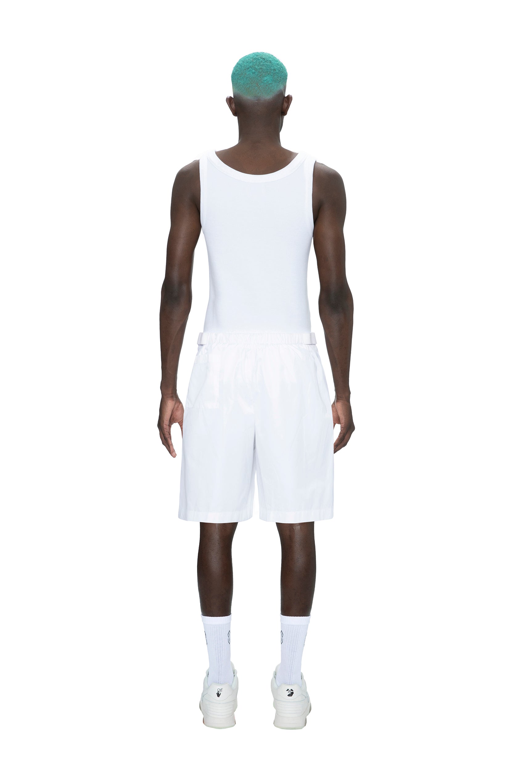 A person with turquoise hair faces away, wearing 6PM TECH SHORTS WHITE, a white tank top, white socks, and white sneakers against a plain white background.