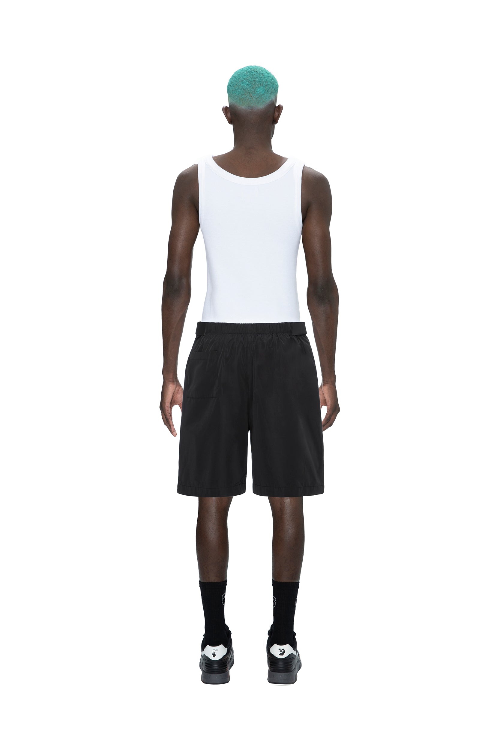 A person with teal hair faces away, wearing a white tank top, 6PM TECH SHORTS BLACK, black socks, and black sneakers, against a plain white background.