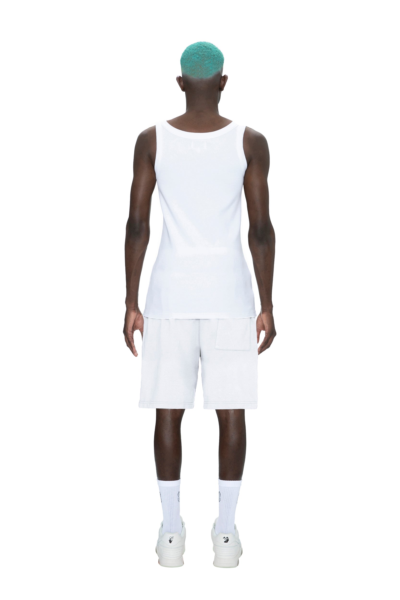 A person with teal hair stands facing away, wearing 6PM SWEATSHORTS WHITE, a white tank top, white socks, and white sneakers against a plain white background.