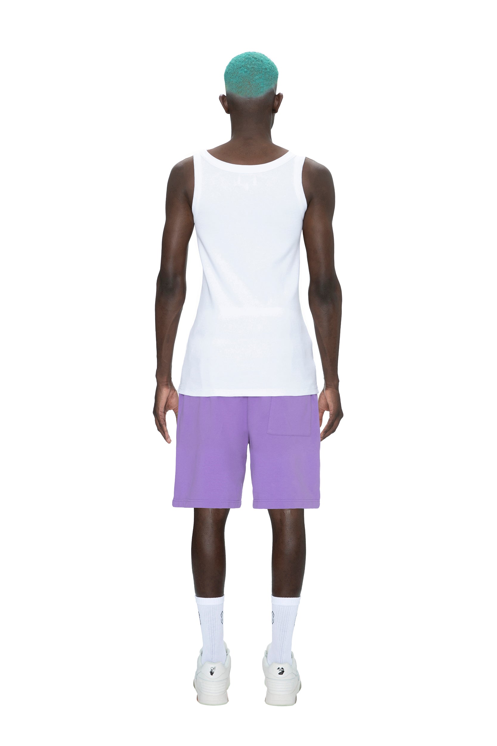 A person with teal hair faces away, wearing a white tank top, 6PM SWEATSHORTS LILAC, white socks, and white sneakers against a plain white background.