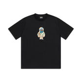 The 6PM MONEY GUY TEE BLACK features a small centered graphic of a cartoon character in a beige parka and blue mask, standing with a neutral expression on a plain white background.