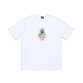 The 6PM MONEY GUY TEE WHITE features a small, colorful cartoon character in a blue hoodie and round glasses holding a teddy bear at the center chest, plus a black logo tag on the neckline.