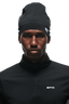 A man wearing the 6PM TECHNICAL LOGO BEANIE and a black zip-up top with 6PM branding looks seriously at the camera against a plain background.