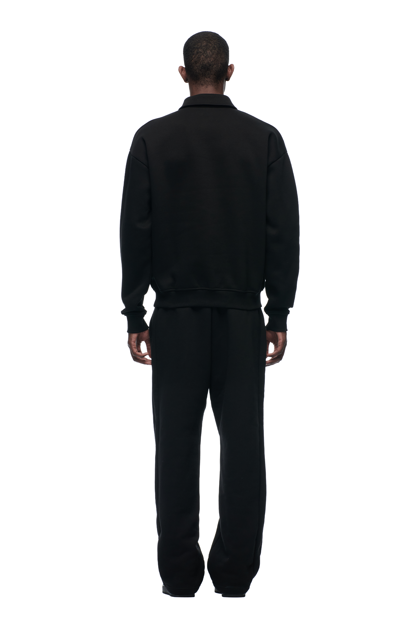 A person stands facing away in a casual, loose-fitting 6PM POLO BLACK jacket and pants against a plain light background.
