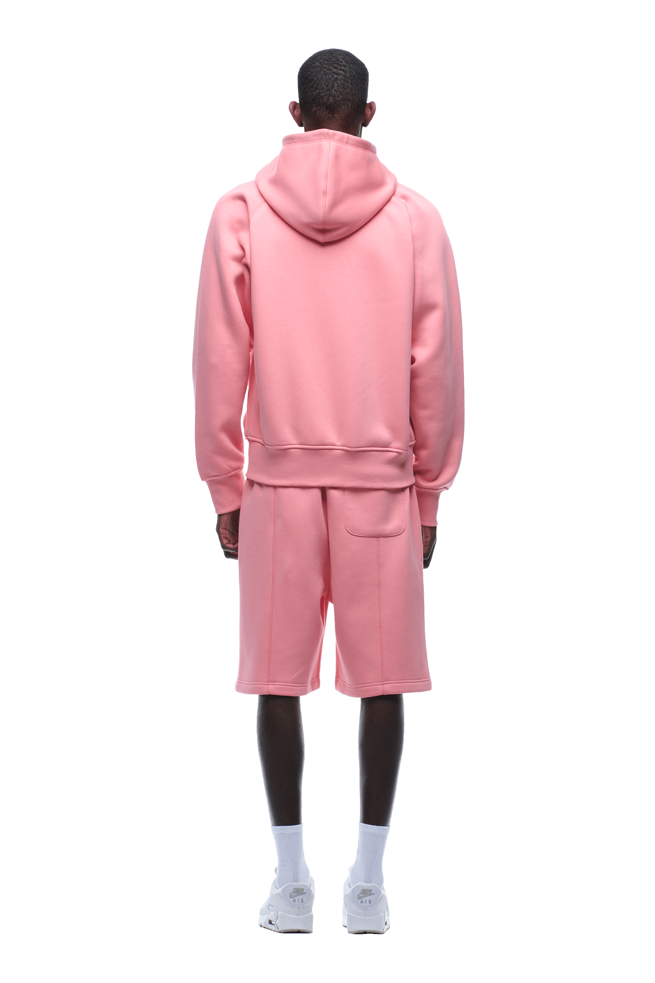 A person stands facing away, wearing the 6PM COVERLOCK ZIP HOODIE FLAMINGO PINK with matching pink shorts, white socks, and white sneakers against a plain background.