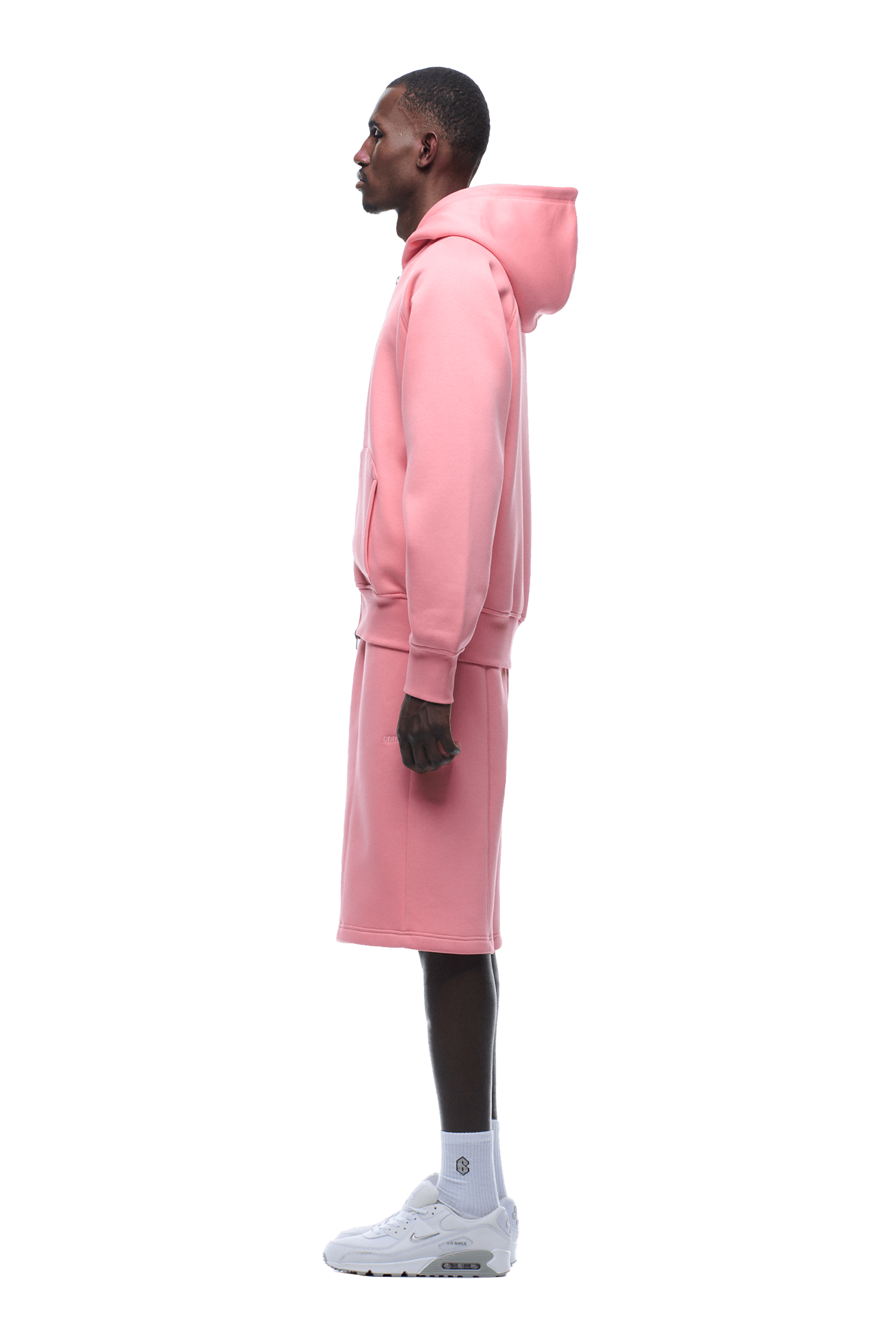 A person in profile faces left, wearing the 6PM COVERLOCK ZIP HOODIE in Flamingo Pink, with matching pink shorts, white socks, and white sneakers on a transparent background.