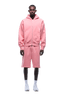 A man faces forward against a plain background, wearing the 6PM COVERLOCK ZIP HOODIE in Flamingo Pink with matching knee-length shorts, paired with white socks and white sneakers.