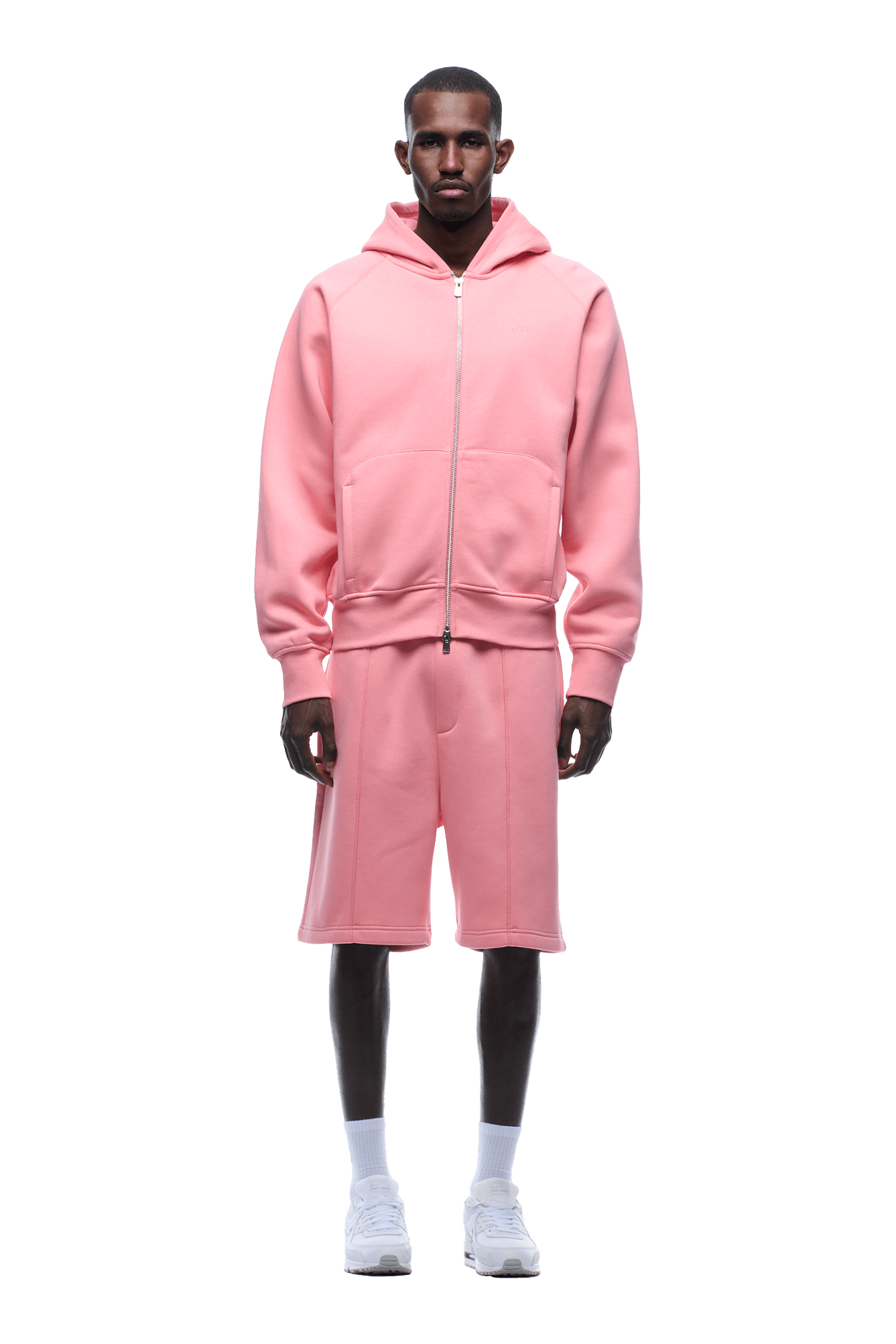 A man faces forward against a plain background, wearing the 6PM COVERLOCK ZIP HOODIE in Flamingo Pink with matching knee-length shorts, paired with white socks and white sneakers.
