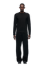 A man stands facing forward against a plain white background, wearing the 6PM CLEAN LONGSLEEVE BLACK shirt, along with black pants and shoes.