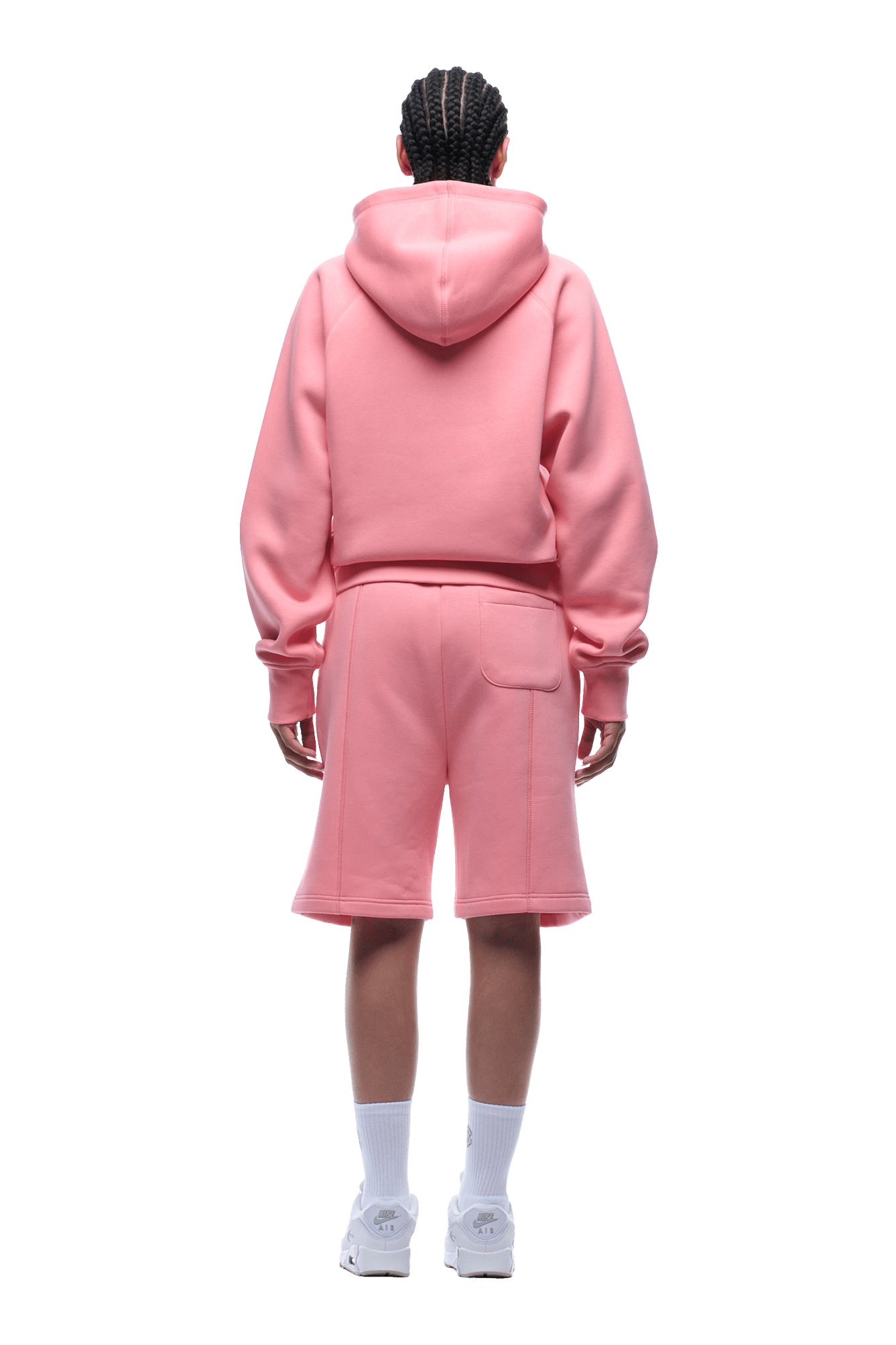 A person with braided hair stands facing away, wearing the 6PM COVERLOCK ZIP HOODIE FLAMINGO PINK, matching pink shorts, white socks, and white sneakers against a transparent background.