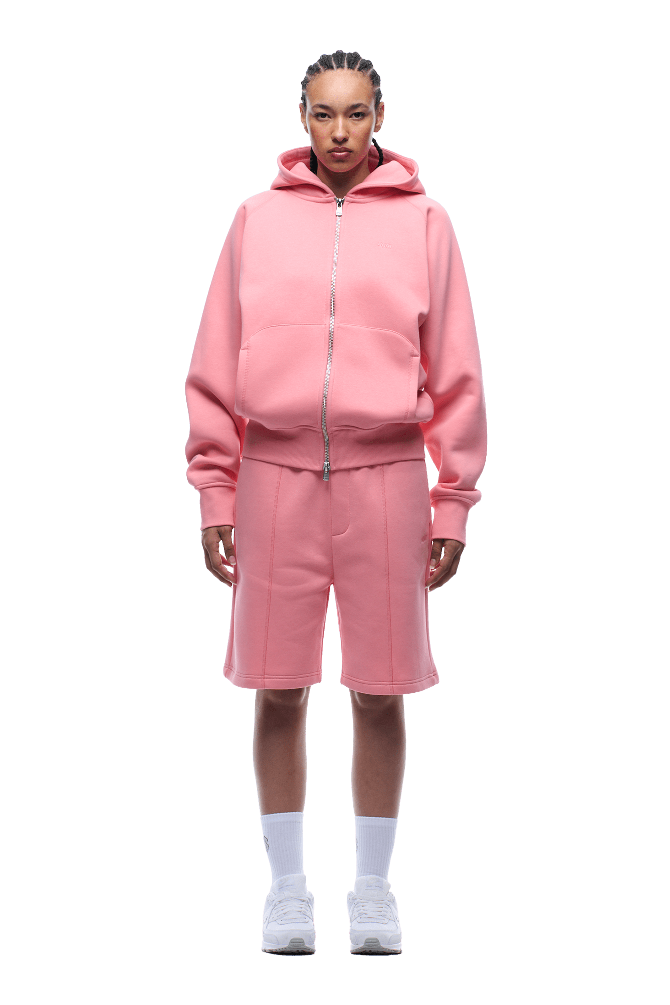 A person stands facing forward in a 6PM COVERLOCK ZIP HOODIE FLAMINGO PINK, paired with matching pink knee-length shorts, white socks, and white sneakers on a transparent background.
