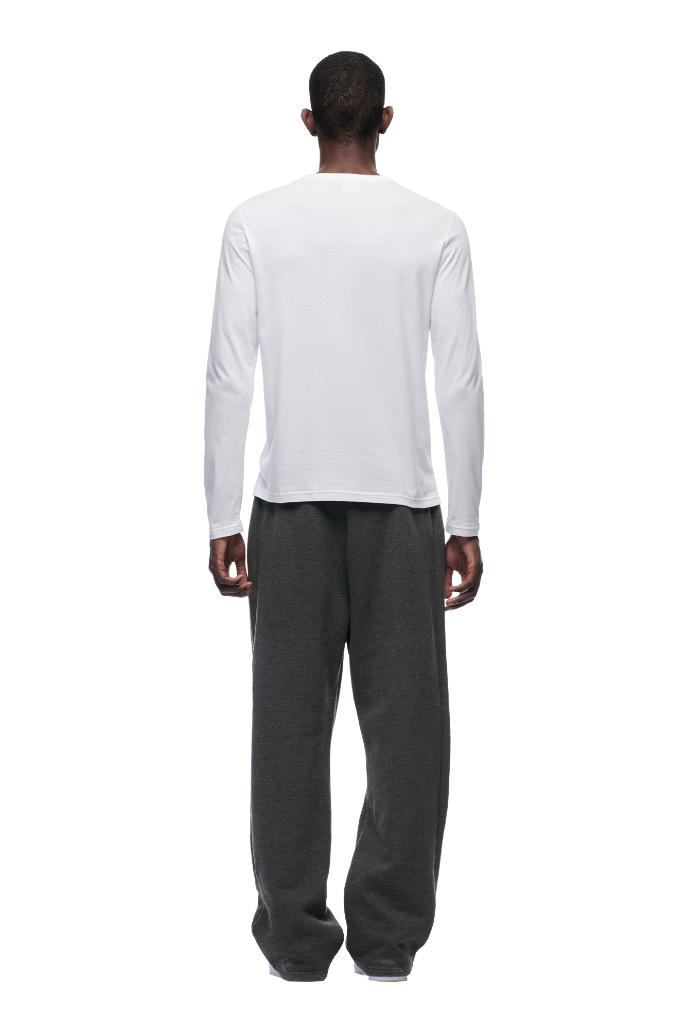 A person stands facing away from the camera, wearing the 6PM CLEAN LONGSLEEVE WHITE shirt and loose dark gray pants, against a plain white background.