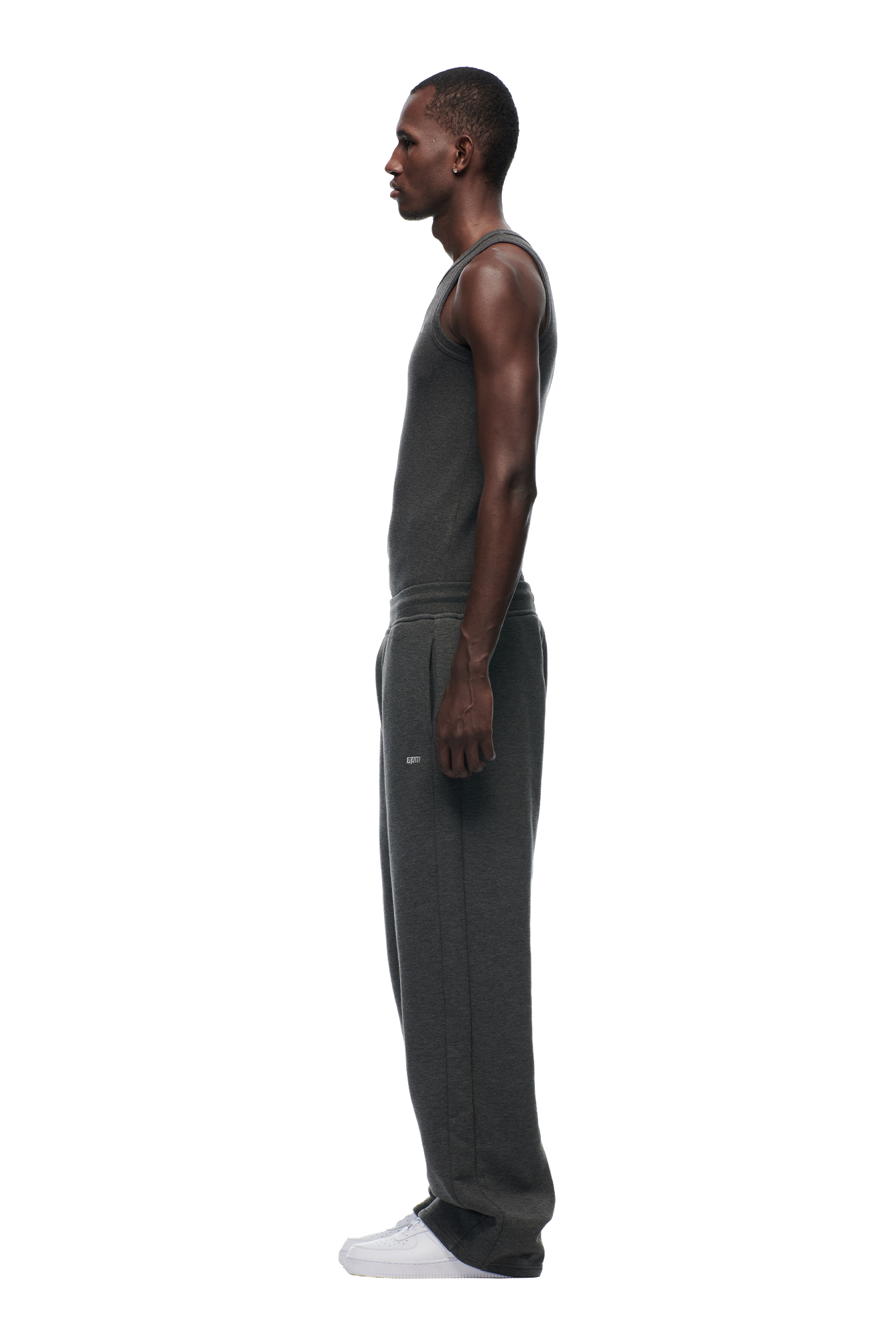 A man stands in profile facing left, dressed in 6PM's OPEN LEG JOGGER DARK GREY MELANGE and a matching dark gray sleeveless tank top with white sneakers, set against a plain white background.