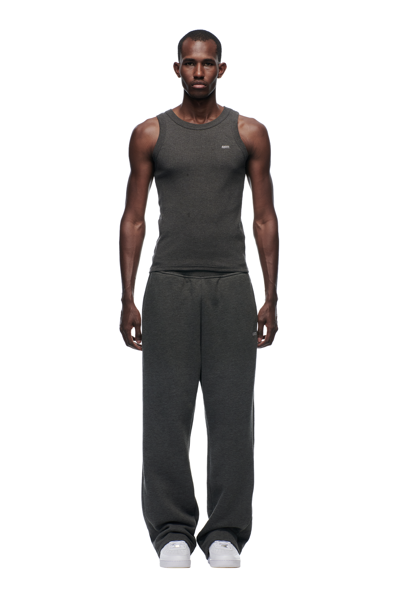 A man faces forward wearing 6PM's OPEN LEG JOGGER DARK GREY MELANGE pants, a fitted dark gray tank top, and white sneakers against a plain white background.