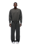 A man stands facing forward wearing the 6PM CREWNECK DARK GREY MELANGE sweatshirt with ribbed trims, matching sweatpants, and white sneakers against a plain white background, his hands resting by his sides.
