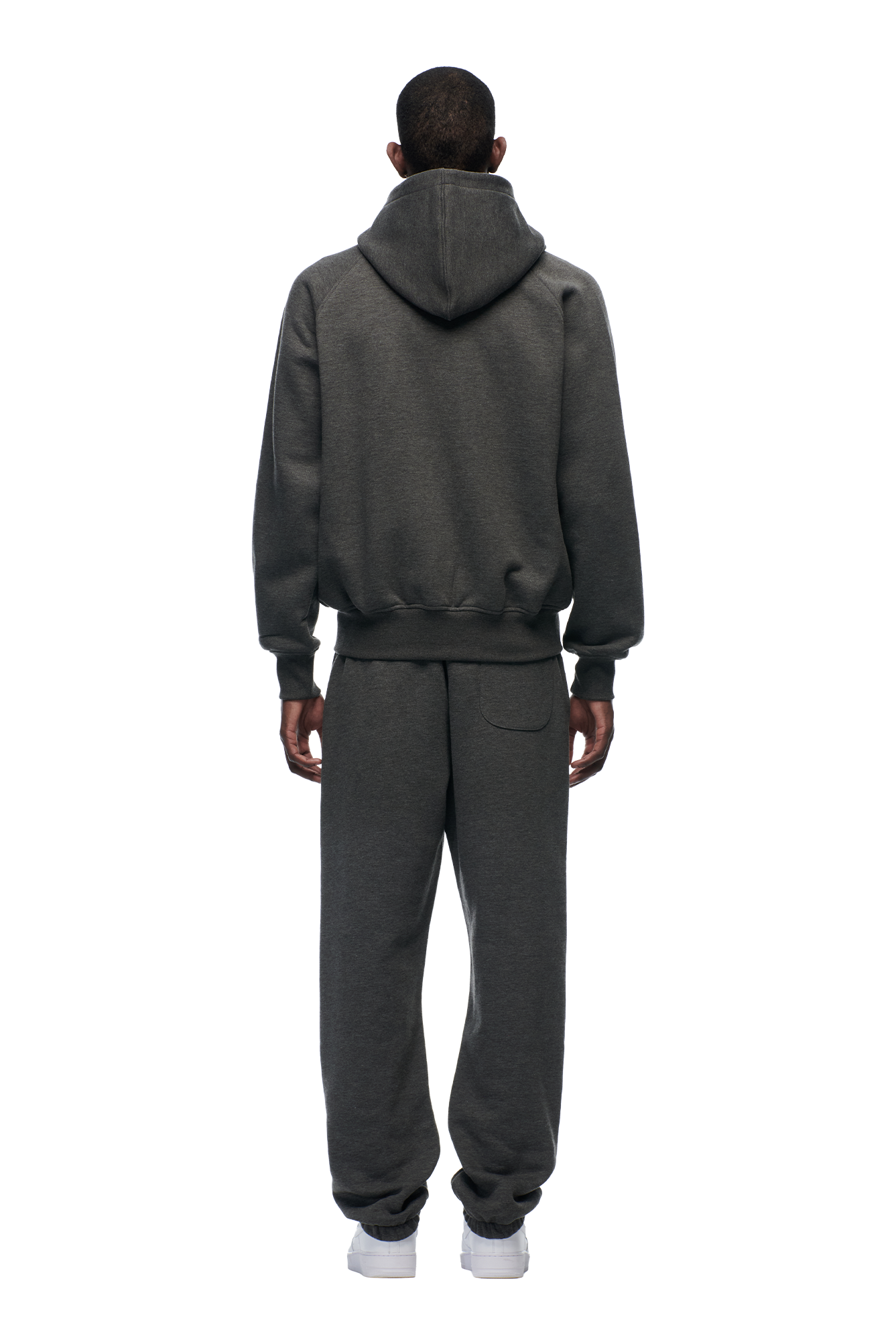 A person faces away from the camera, wearing the 6PM ZIP HOODIE DARK GREY MELANGE and matching sweatpants with white sneakers, set against a plain white background.