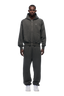 A man faces forward against a plain white background, wearing the 6PM ZIP HOODIE DARK GREY MELANGE with matching sweatpants and white sneakers.