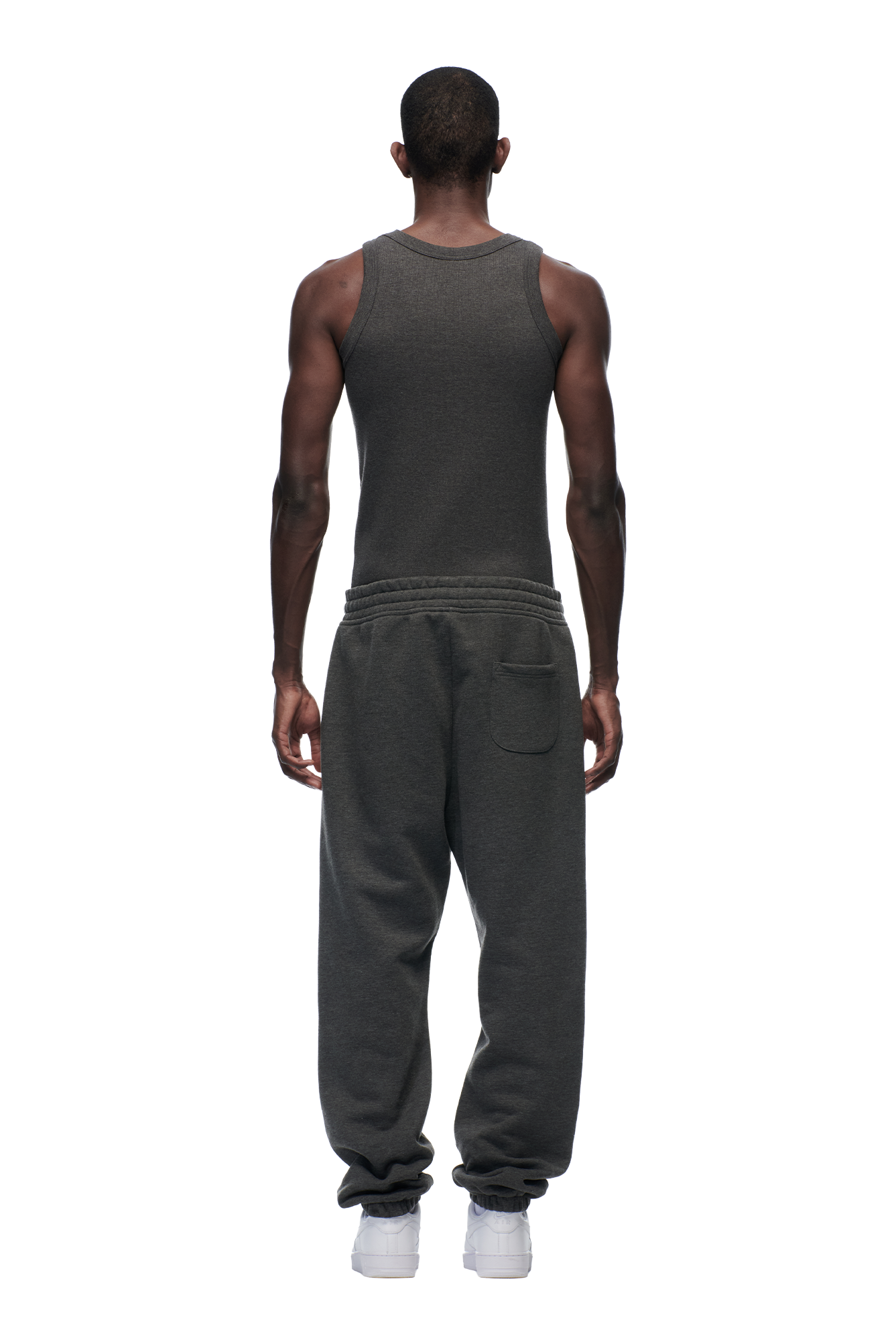 A man faces away from the camera, wearing 6PM's CUFF JOGGER DARK GREY MELANGE sweatpants with a matching dark gray tank top and white sneakers, set against a plain white background.