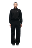 A person stands facing forward, wearing the 6PM WMNS POLO BLACK collared sweatshirt and loose black pants with black shoes against a plain white background.