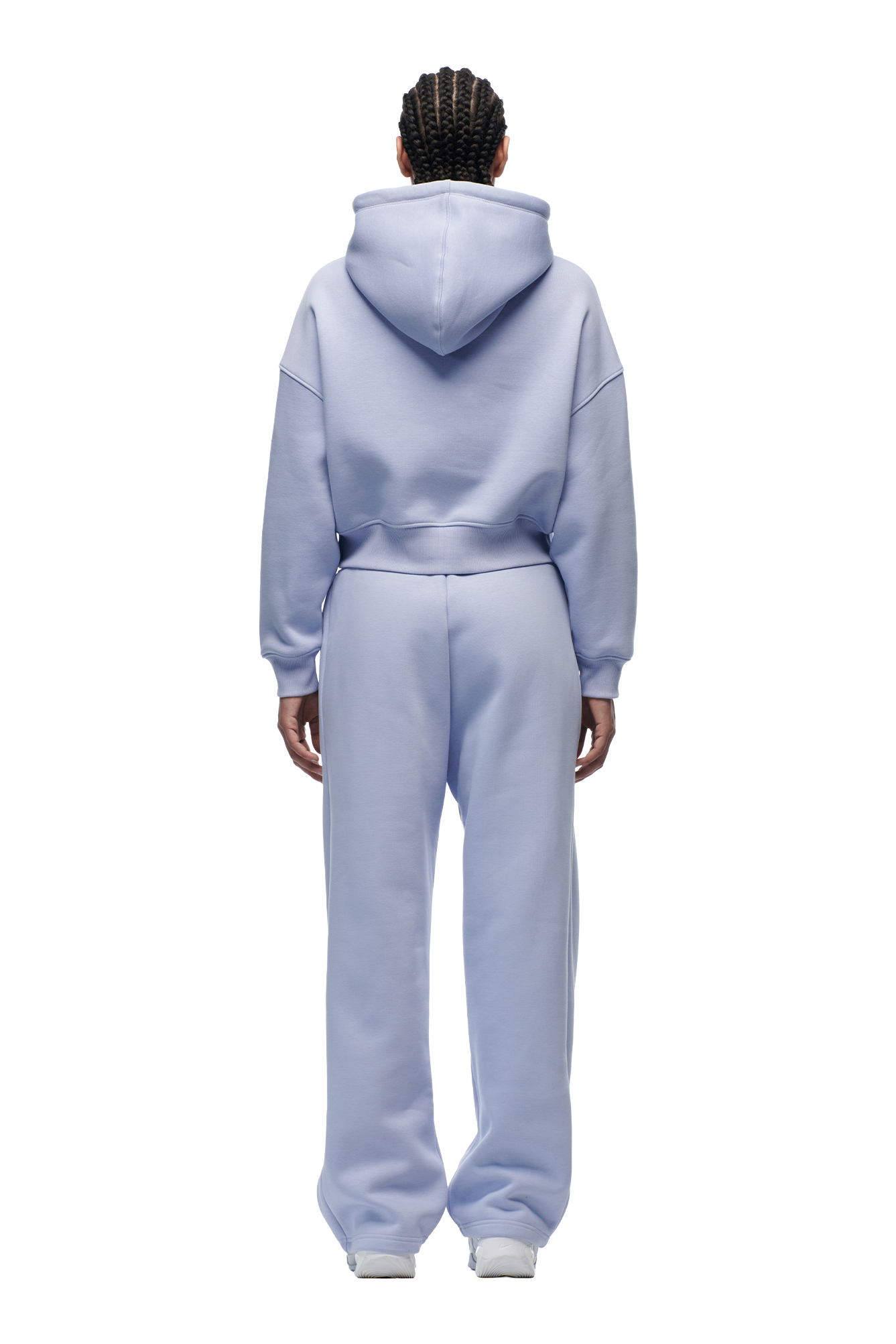 A person with braided hair stands facing away, wearing the 6PM WMNS Cropped Hoodie in Soft Violet and matching sweatpants with white shoes, set against a plain white background.