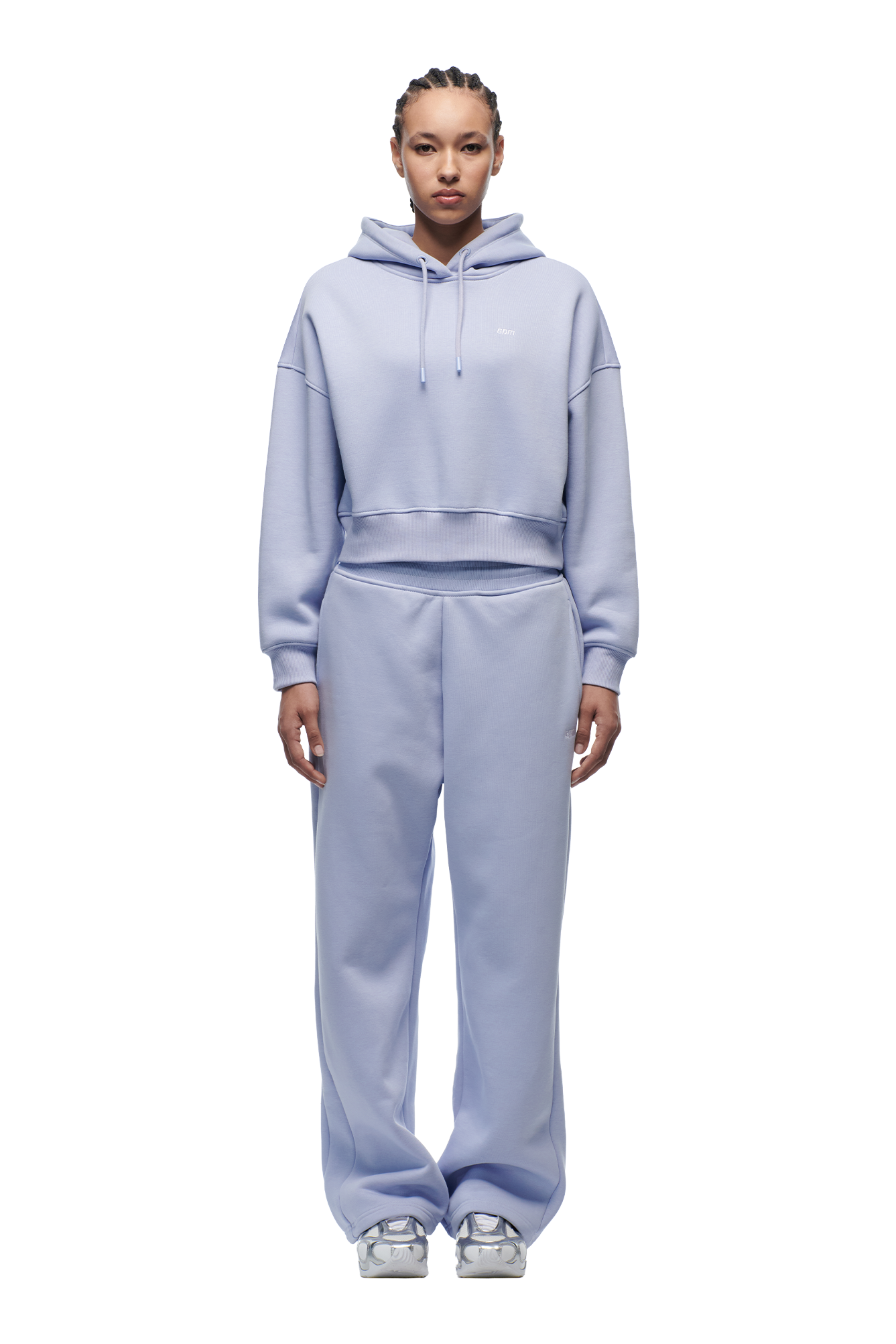 A person faces forward against a white background, wearing the 6PM WMNS CROPPED HOODIE SOFT VIOLET with matching wide-leg sweatpants and silver sneakers.