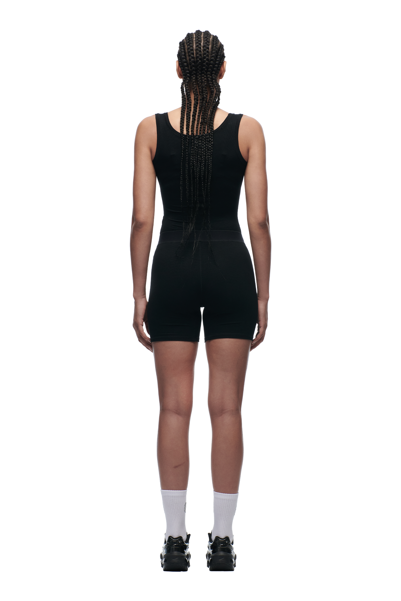 A woman with long braids stands facing away against a plain white background, wearing the 6PM WMNS TANKTOP BLACK, fitted shorts, white socks, and black sneakers.