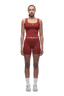A woman faces forward against a white background, wearing 6PM WMNS BOXER SHORTS in wine red with a matching tank top, paired with white socks and sneakers.