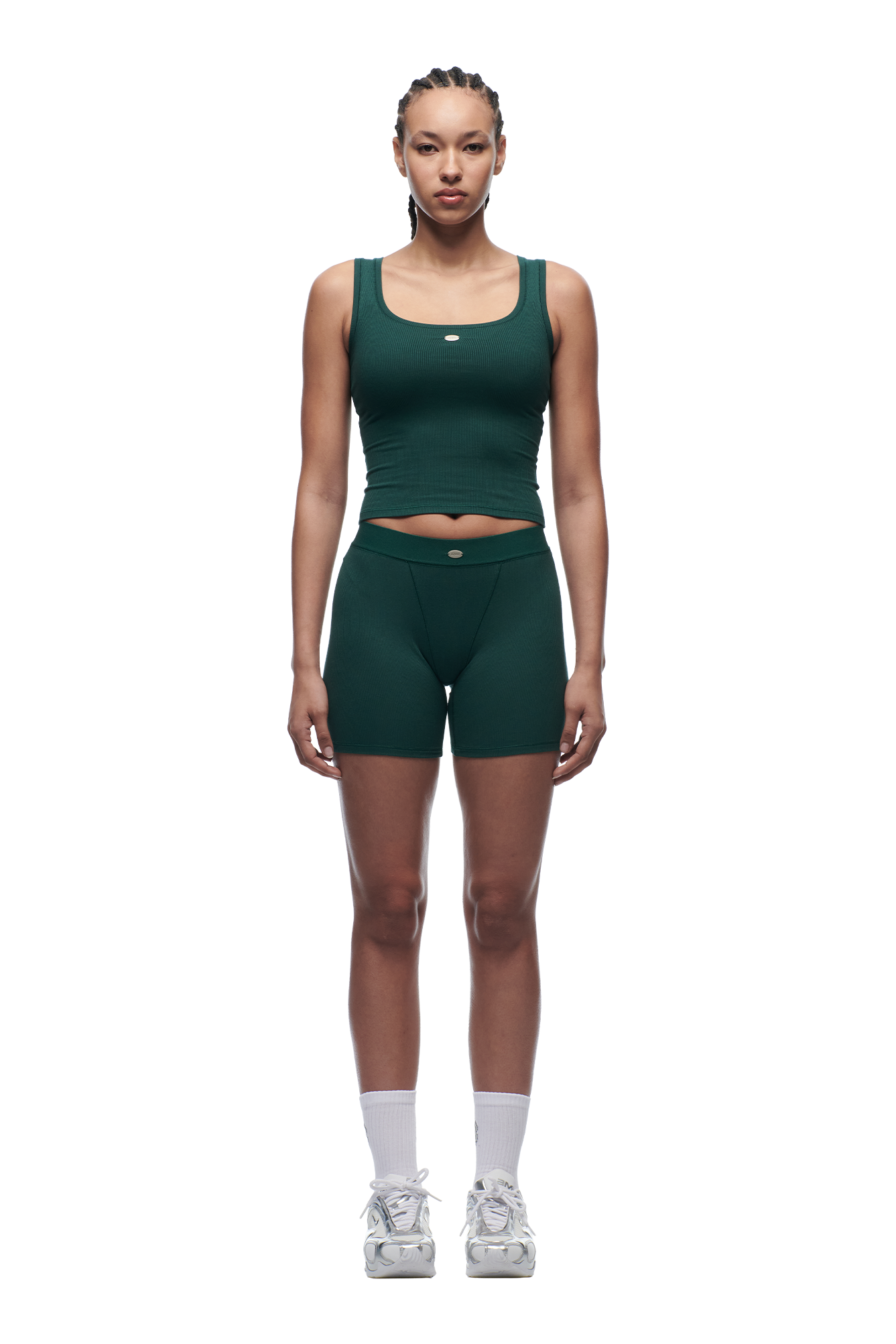 A woman with braided hair faces forward wearing 6PM WMNS BOXER SHORTS EVERGREEN, a green fitted tank and high-waisted shorts set, paired with white socks and gray sneakers against a plain white background.