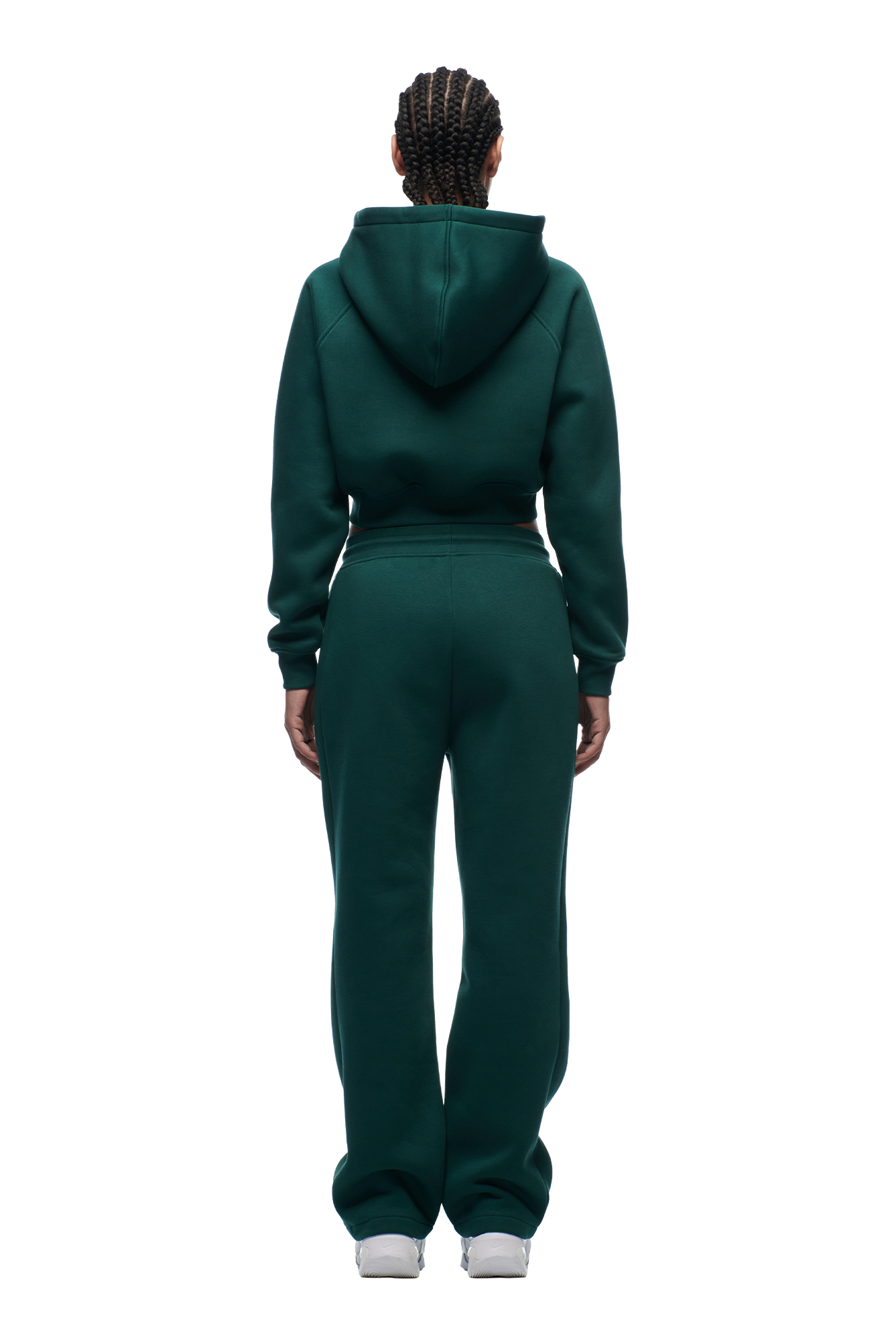A person with braided hair is seen from the back, wearing the 6PM WMNS Cropped Zip Hoodie Evergreen and matching pants, along with white sneakers, standing against a plain white background.
