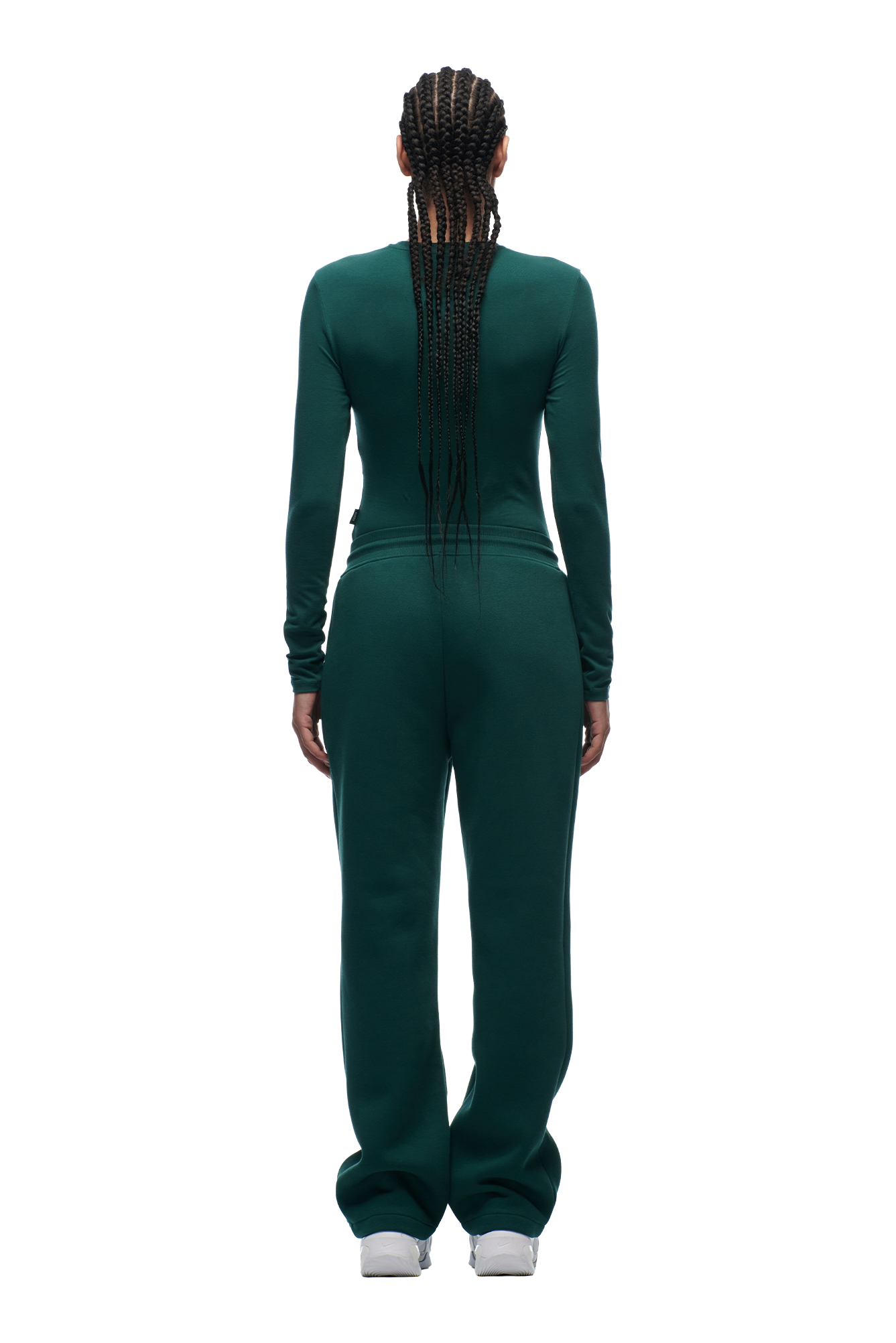 A person with long, braided hair stands facing away on a white background, wearing the 6PM WMNS LONGSLEEVE EVERGREEN top and matching pants with gray sneakers.
