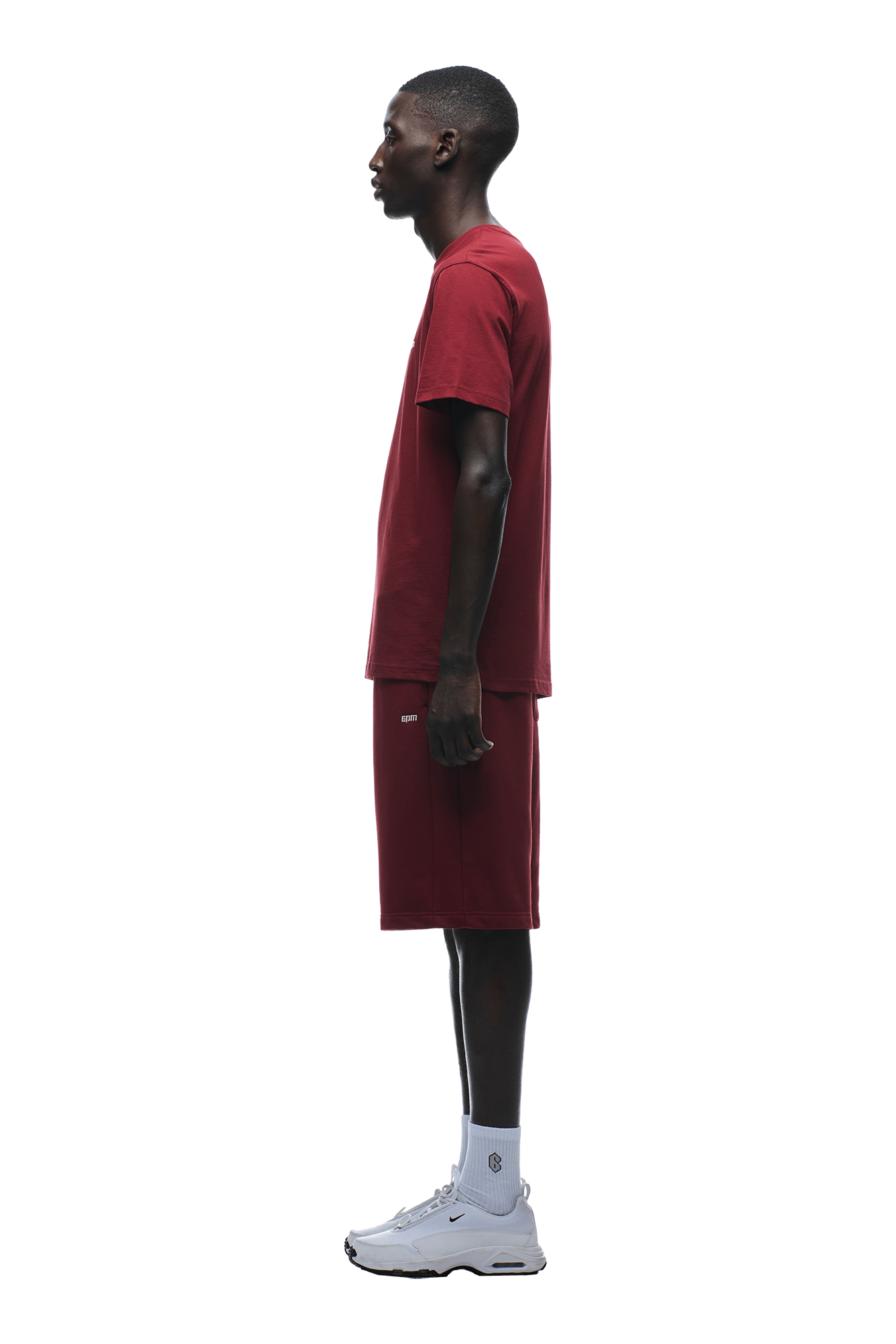 A young man stands in profile against a green background, wearing the 6PM T-SHIRT REGULAR FIT WINE RED with matching shorts, paired with white socks and athletic shoes.