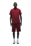 A man stands facing forward in a matching 6PM T-SHIRT REGULAR FIT WINE RED and shorts set, paired with white socks and sneakers, showing how a simple look can stand out against a green background.