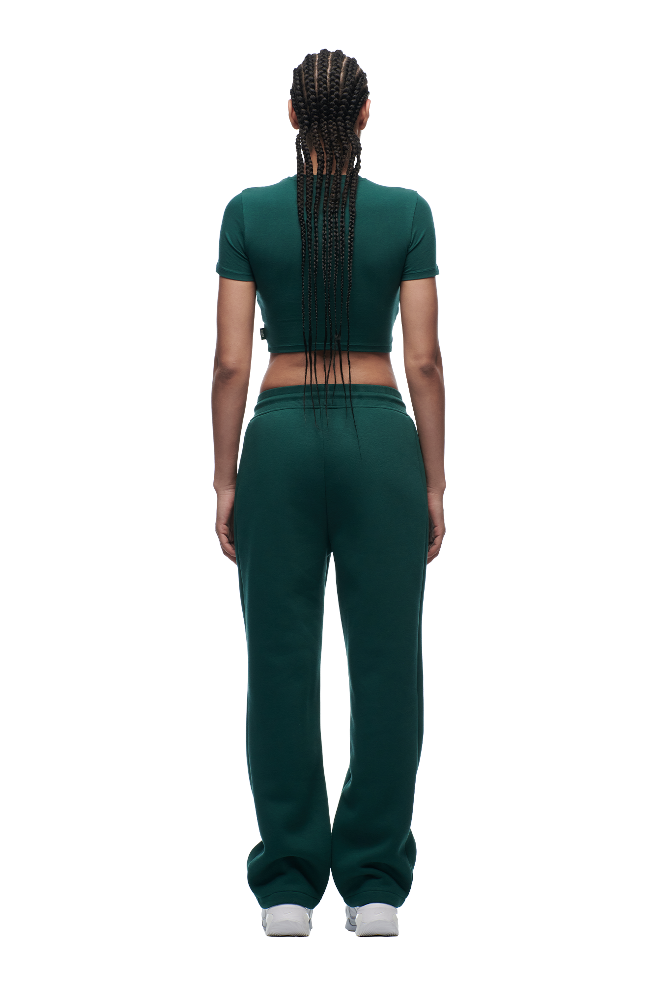 A person with braided hair is seen from behind, wearing the 6PM WMNS CROPPED T-SHIRT EVERGREEN and matching sweatpants with white sneakers against a plain white background.