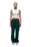 A person stands facing forward wearing 6PM's WMNS OPEN LEG EVERGREEN dark green sweatpants with a drawstring, paired with a white sleeveless crop top and gray sneakers, against a plain white background.