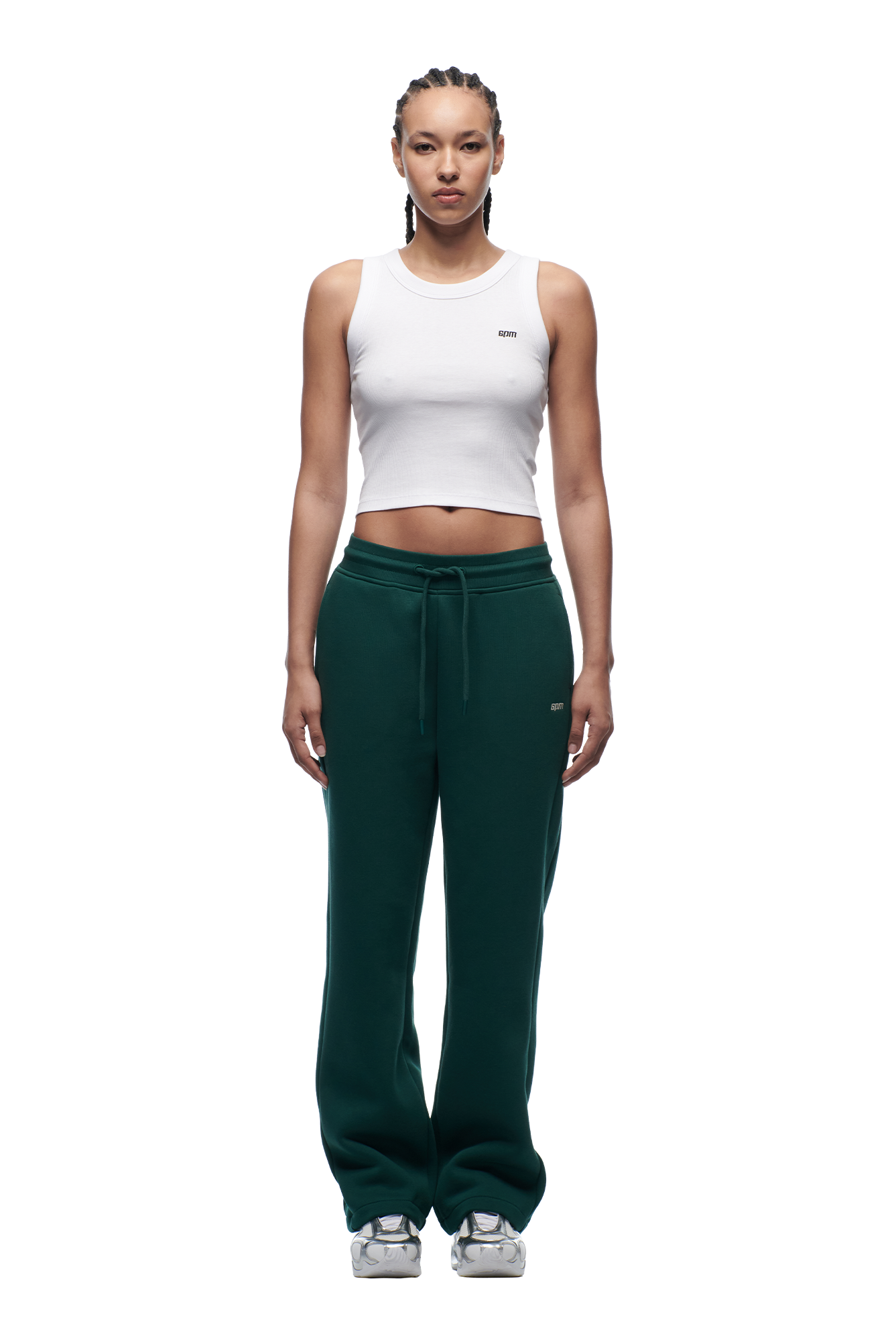 A person stands facing forward wearing 6PM's WMNS OPEN LEG EVERGREEN dark green sweatpants with a drawstring, paired with a white sleeveless crop top and gray sneakers, against a plain white background.