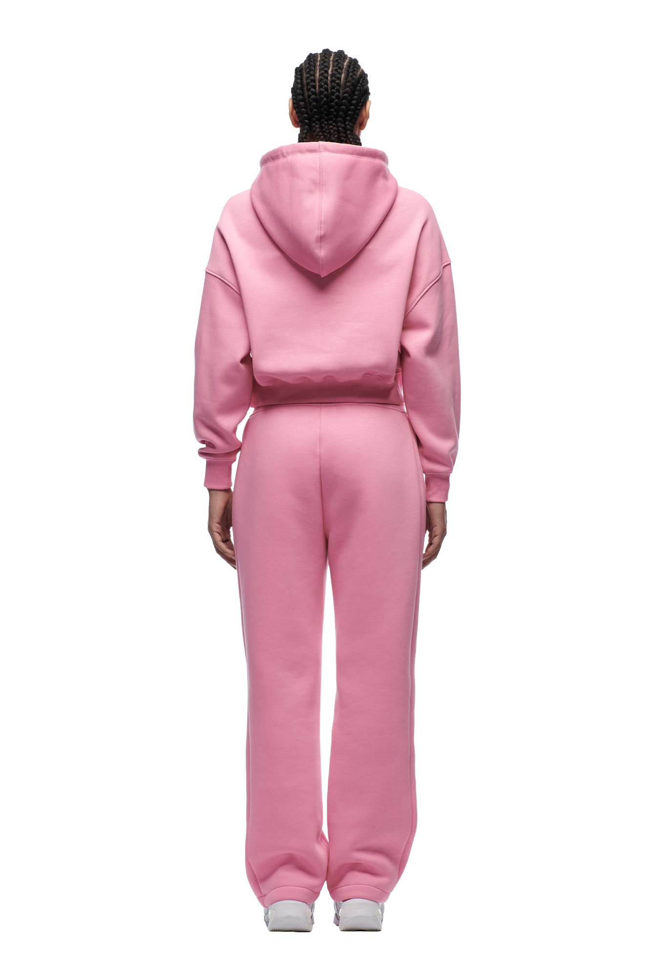 A person with braided hair stands facing away against a white background, wearing the 6PM WMNS CROPPED HOODIE BUBBLEGLOW and matching sweatpants with white sneakers.