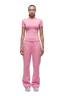 A person with braided hair faces forward, wearing the 6PM WMNS T-SHIRT BUBBLEGLOW, loose pink sweatpants with a drawstring, and white sneakers against a plain white background.