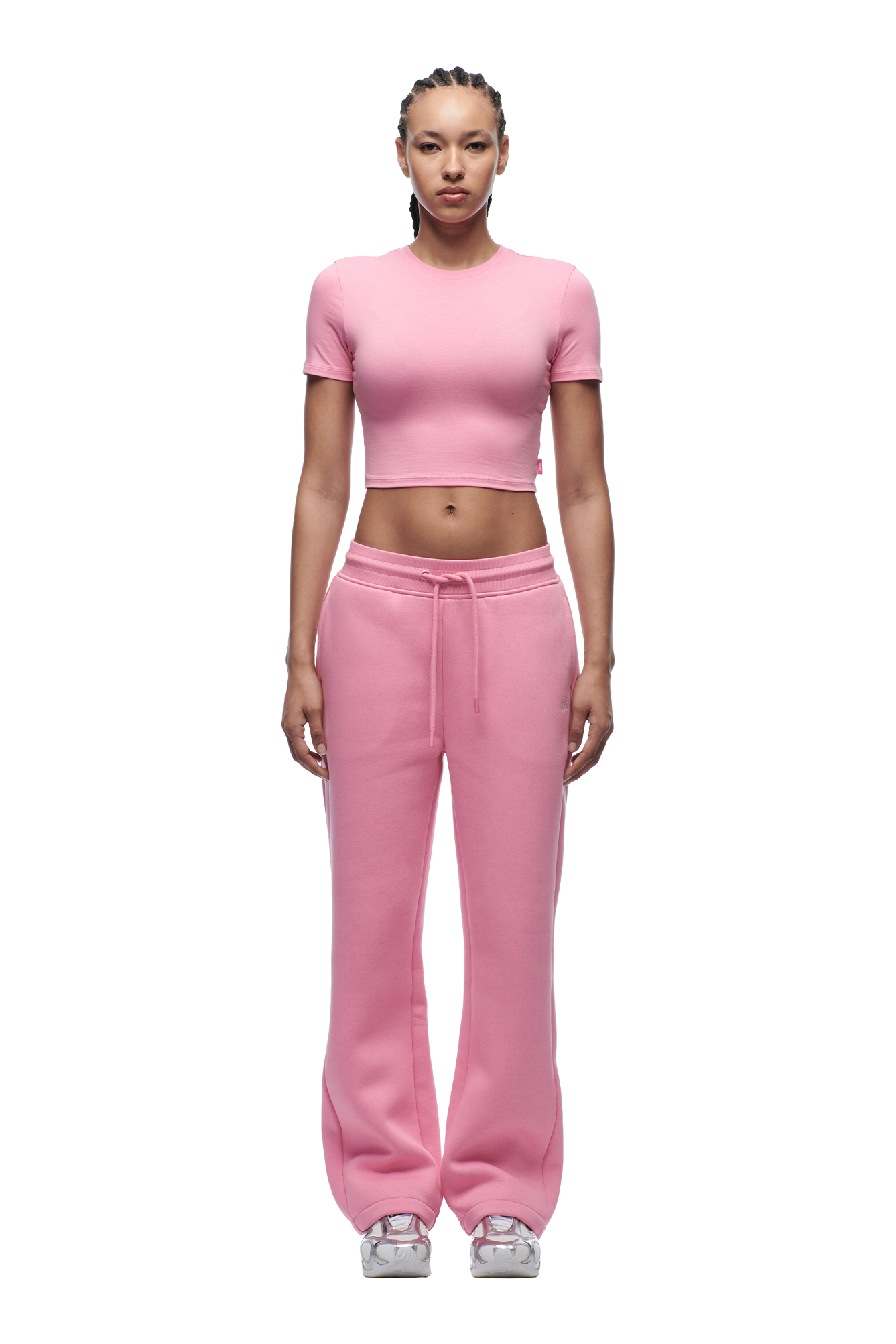 A person faces forward against a plain white background, wearing the 6PM WMNS CROPPED T-SHIRT BUBBLEGLOW with loose pink sweatpants and white sneakers.