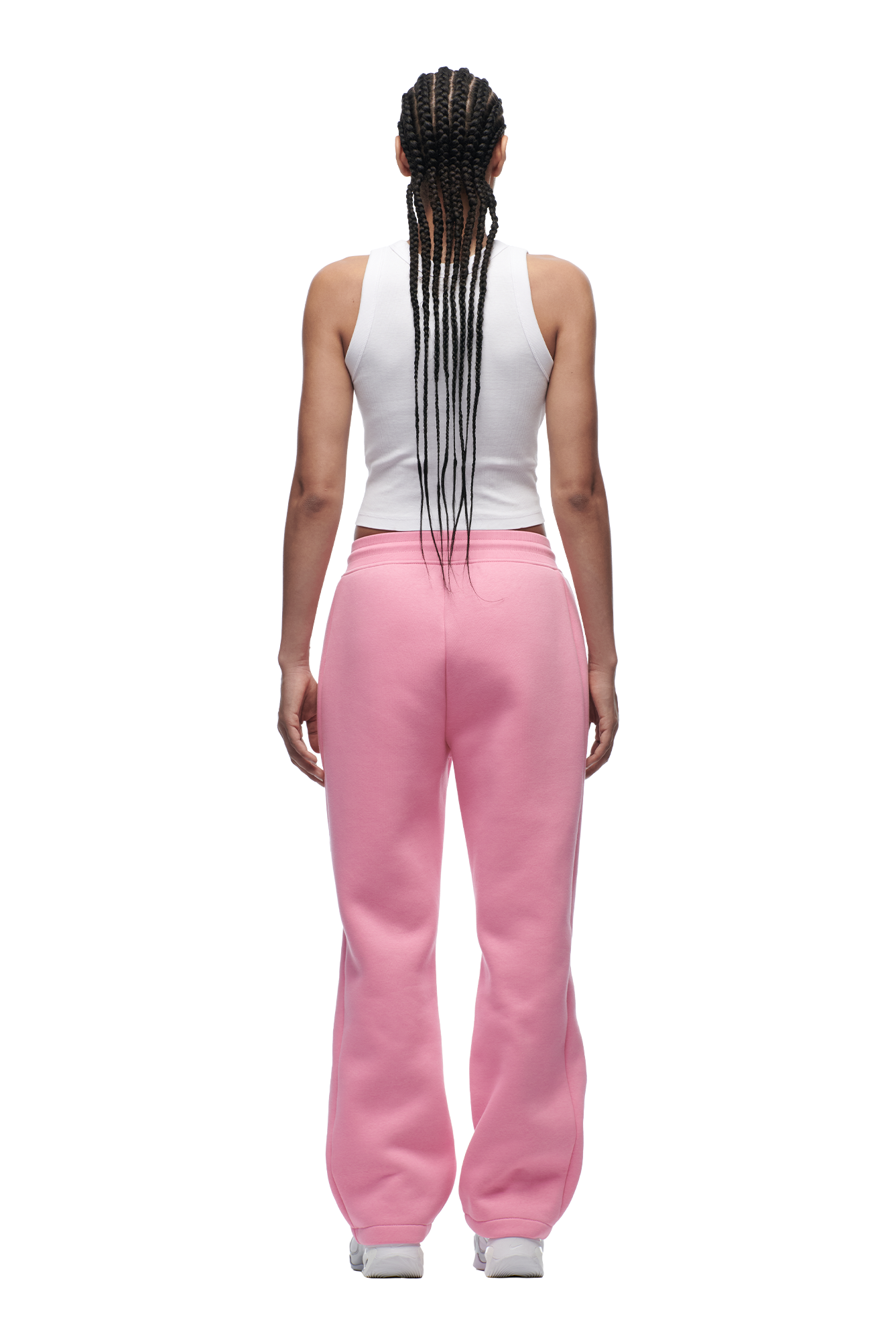 A person with long braided hair faces away, wearing the 6PM WMNS OPEN LEG BUBBLEGLOW pink sweatpants paired with a white sleeveless top and white sneakers, set against a plain white background.
