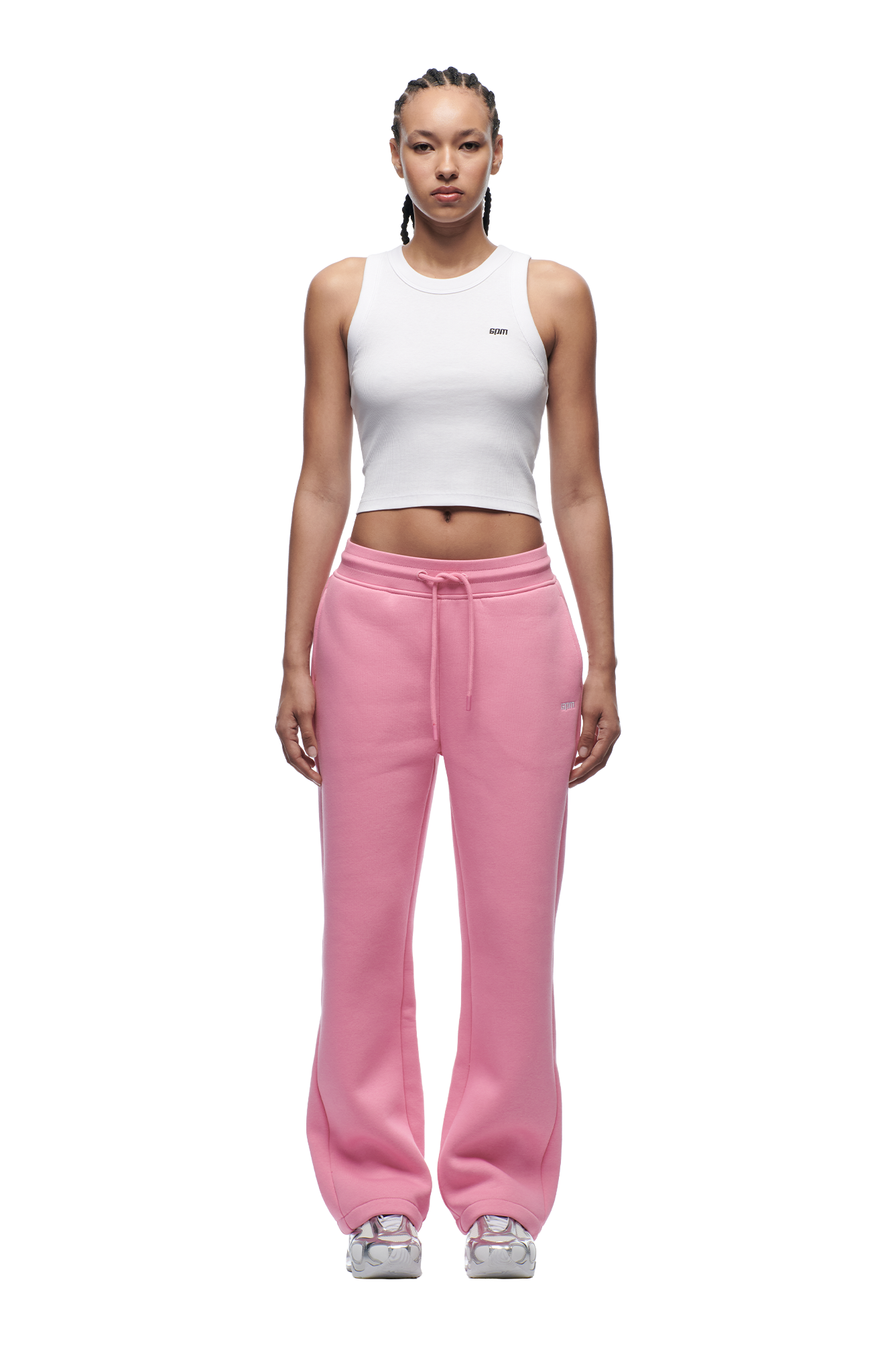 A woman faces forward against a white background, wearing 6PM's WMNS OPEN LEG BUBBLEGLOW pink drawstring sweatpants, a white cropped tank top, and white sneakers.