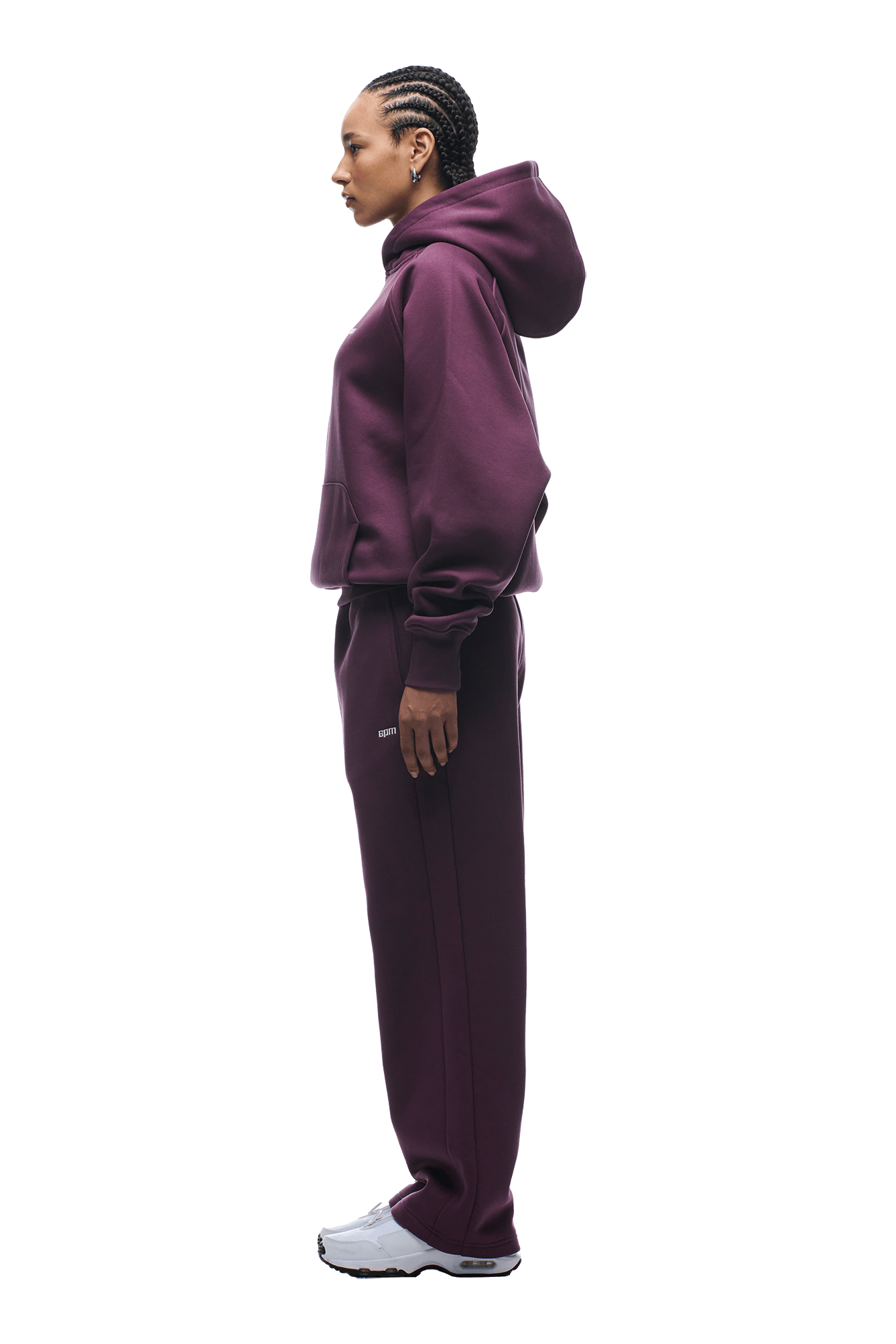 A person stands in profile wearing the 6PM HOODIE PLUM raglan-sleeved hoodie with kangaroo pocket and matching sweatpants, paired with white sneakers, ideal for everyday wear, against a plain background.