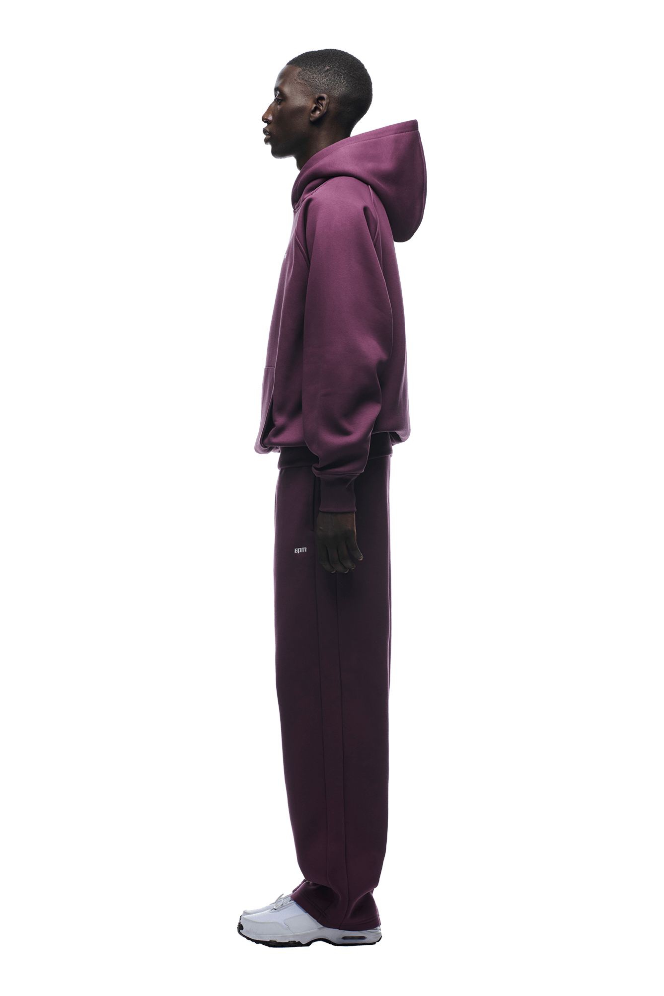 A person in profile wears the 6PM HOODIE PLUM—a matching maroon raglan-sleeved hoodie with kangaroo pocket and sweatpants—paired with white sneakers, posed against a plain green background.