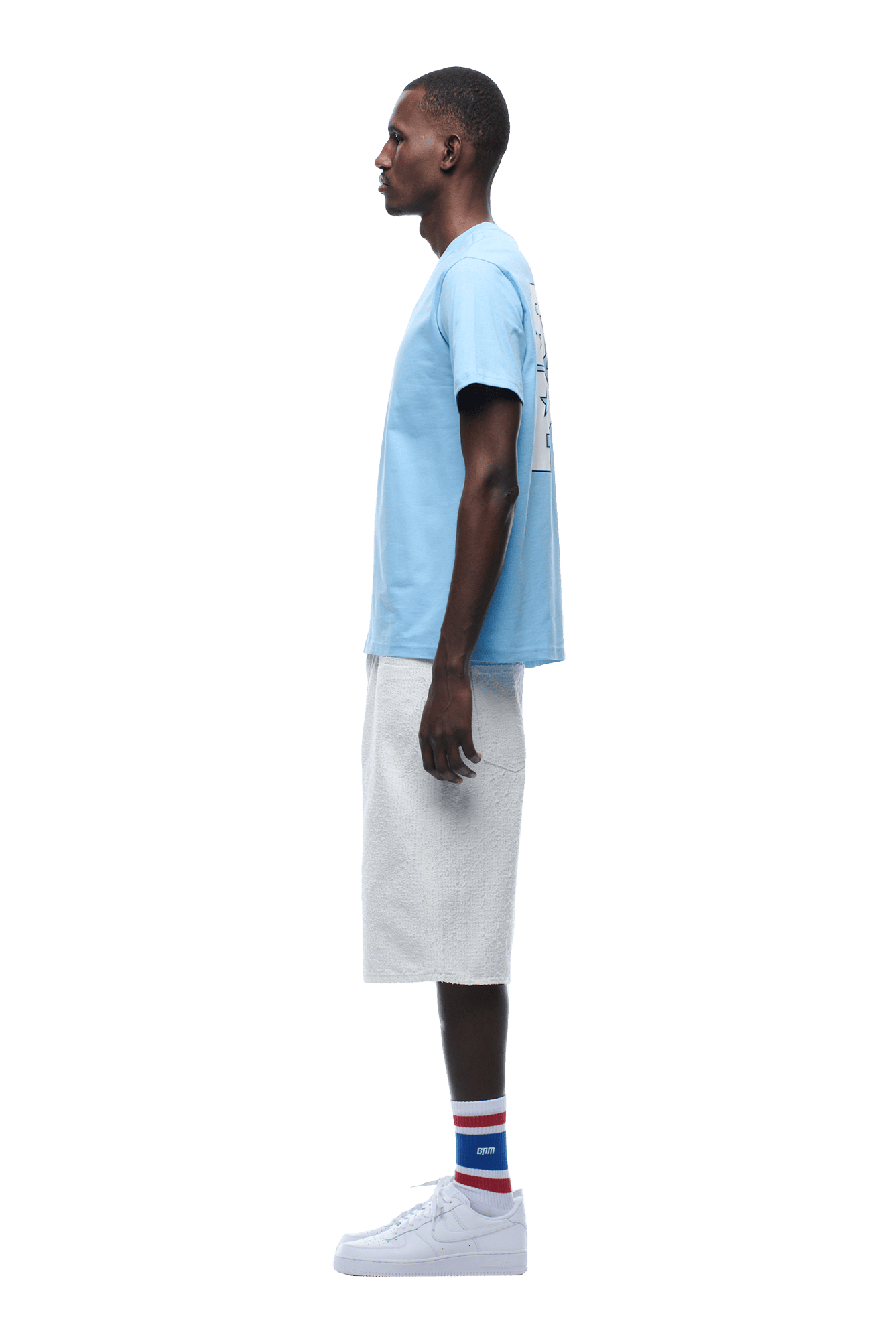 A man in profile faces left, wearing the 6PM COLLEGE STAR TEE BLUE, white knee-length shorts, white sneakers, and striped socks in red, blue, and white. The background is transparent.