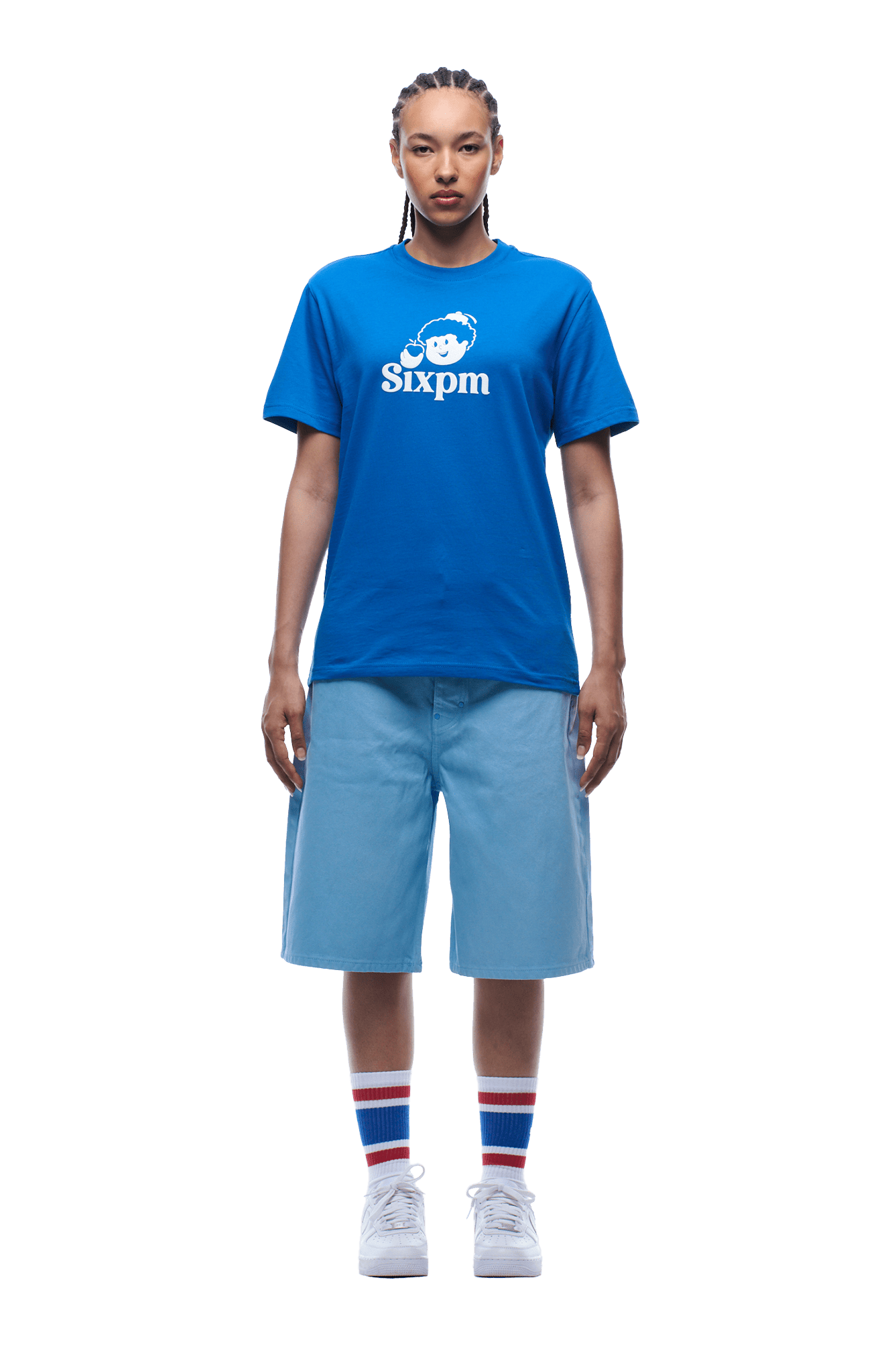 A person with braided hair faces forward, wearing a 6PM APPLE BOY TEE BLUE, light blue knee-length shorts, striped socks, and white sneakers on a transparent background.
