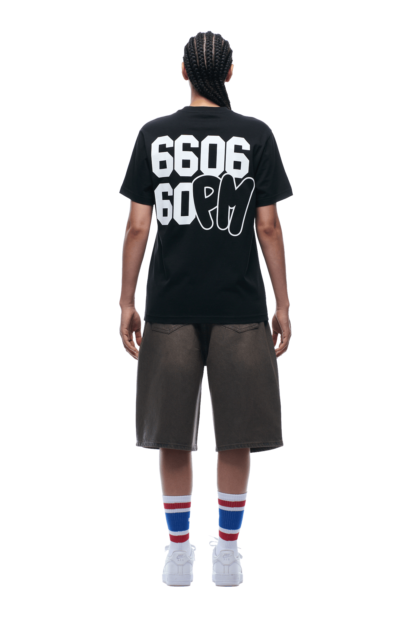 A person with braided hair, wearing the 6PM 660660 TEE BLACK with bold white numbers and letters on the back, paired with dark shorts, white sneakers, and striped socks, is standing facing away from the camera.