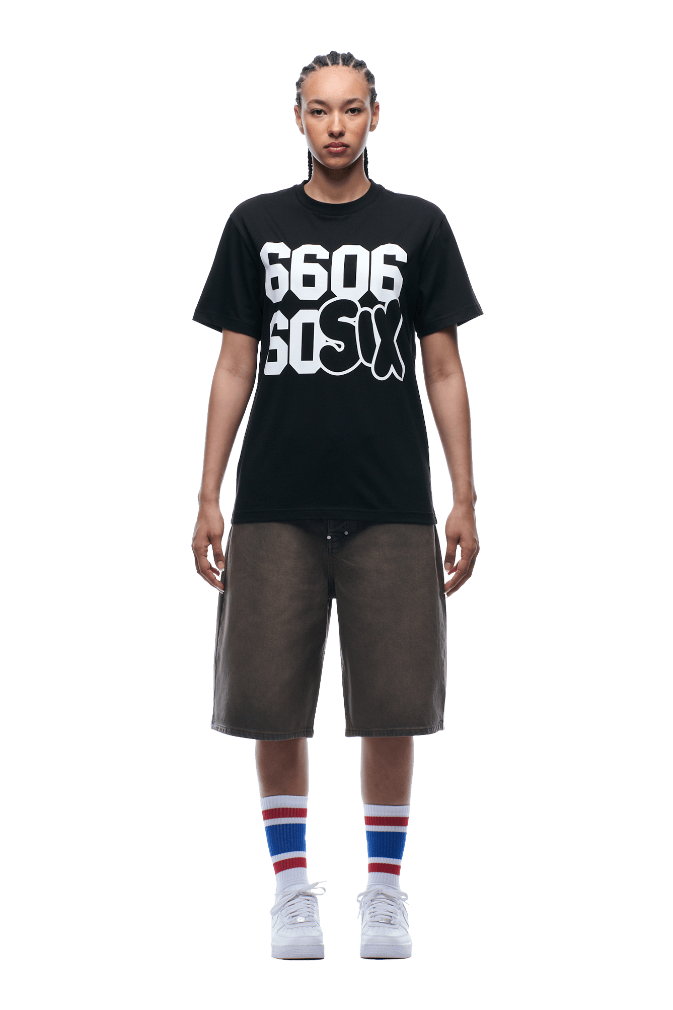 A person with braided hair wears the 6PM 660660 TEE BLACK, paired with long dark shorts, white sneakers, and striped socks, standing against a plain background.