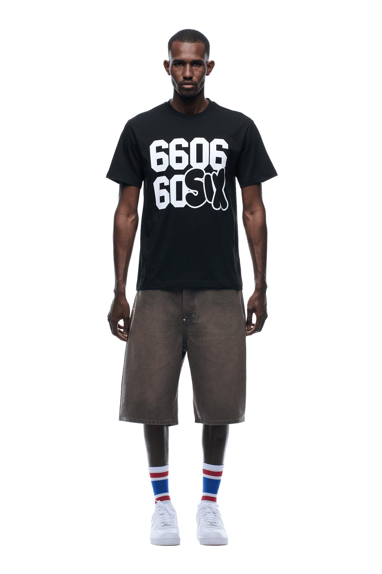 A man faces forward wearing the 6PM 660660 TEE BLACK, long brown shorts, white sneakers, and striped socks; background is transparent.