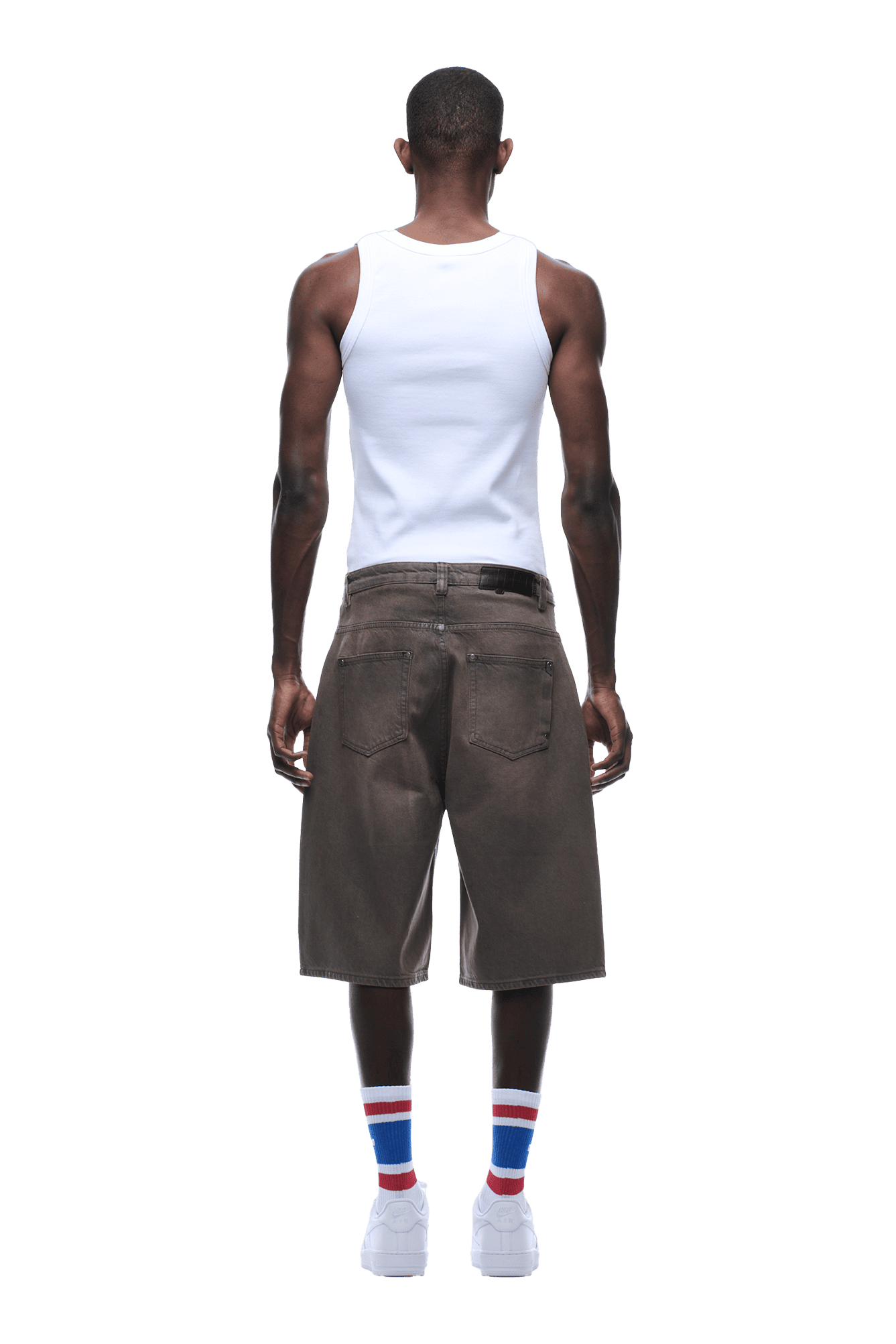 A man stands facing away, wearing a white tank top, 6PM COATED DENIM SHORTS WASHED BROWN, white sneakers, and white socks with red and blue stripes. The background is transparent.